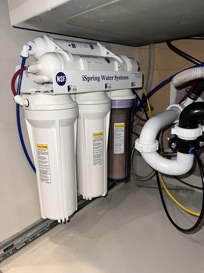 A reverse osmosis system installed under a kitchen sink, with filter housings and tubing neatly routed.