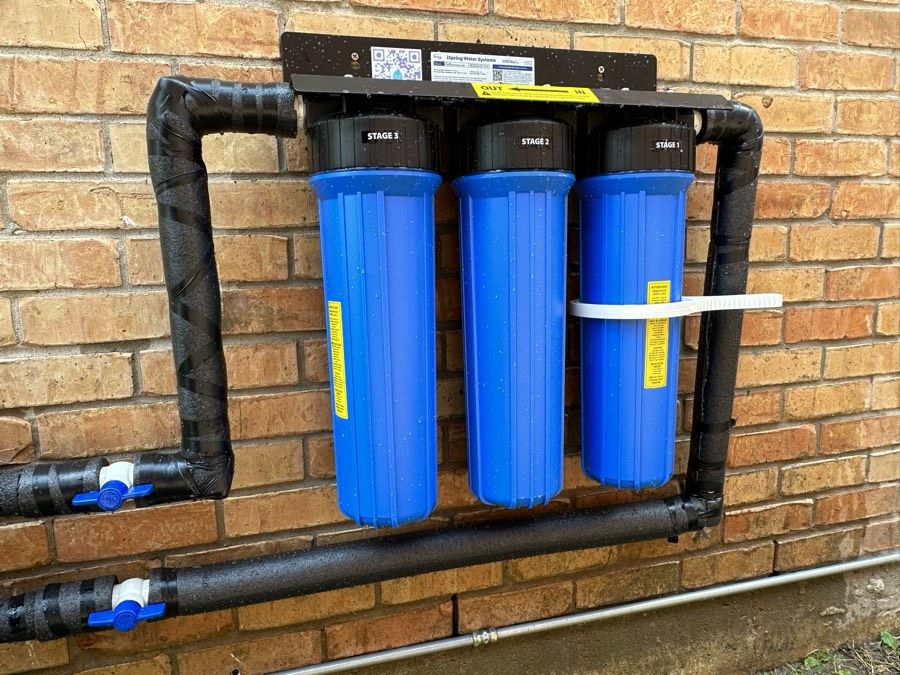 A three-stage Mrs. Water system mounted on a brick wall, with black insulated piping and shut-off valves.